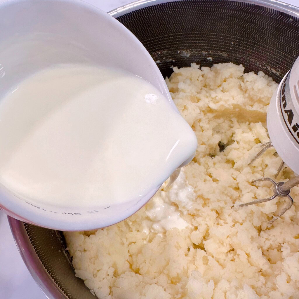 Adding the warmed cream to the mashed potatoes.