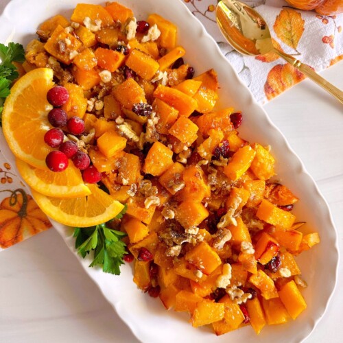 White platter filled with roasted butternut squash, fresh cranberries, and candied pecans.