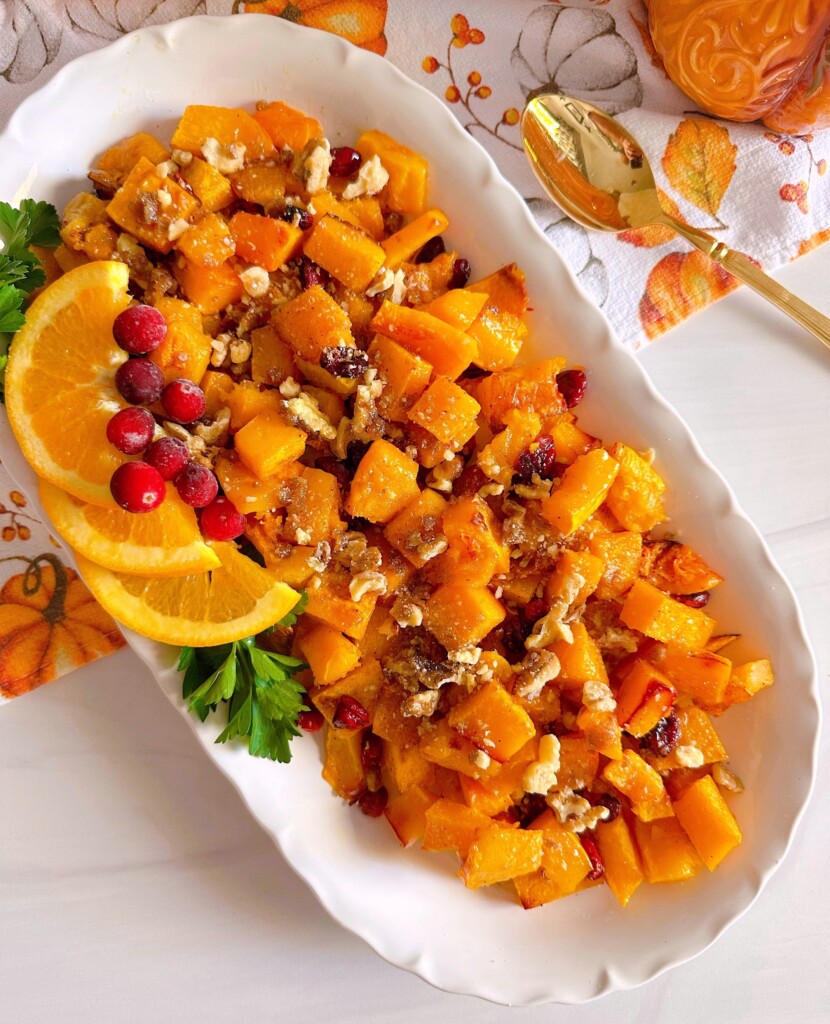 White platter filled with roasted butternut squash, fresh cranberries, and candied pecans.
