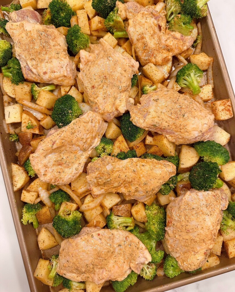 Chicken thighs placed on top of the vegetables on the sheet pan.