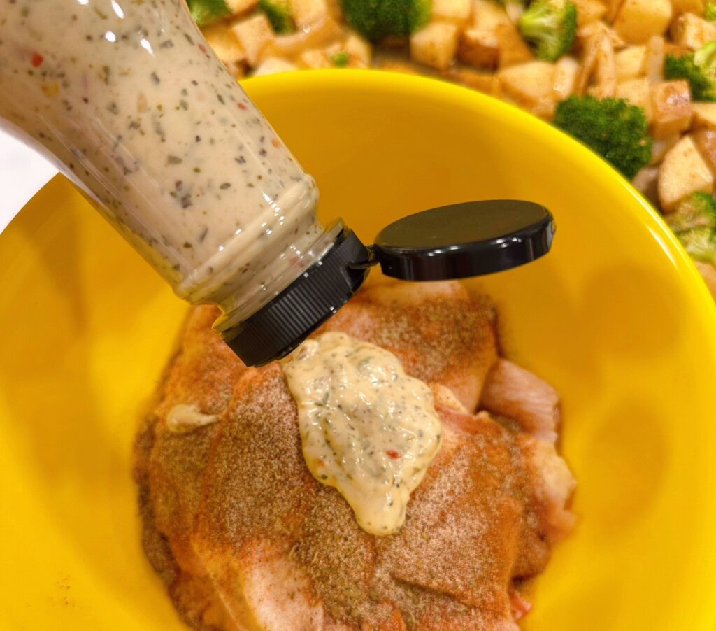 Adding the Wingers Garlic Parmesan Sauce to the chicken in a yellow bowl.