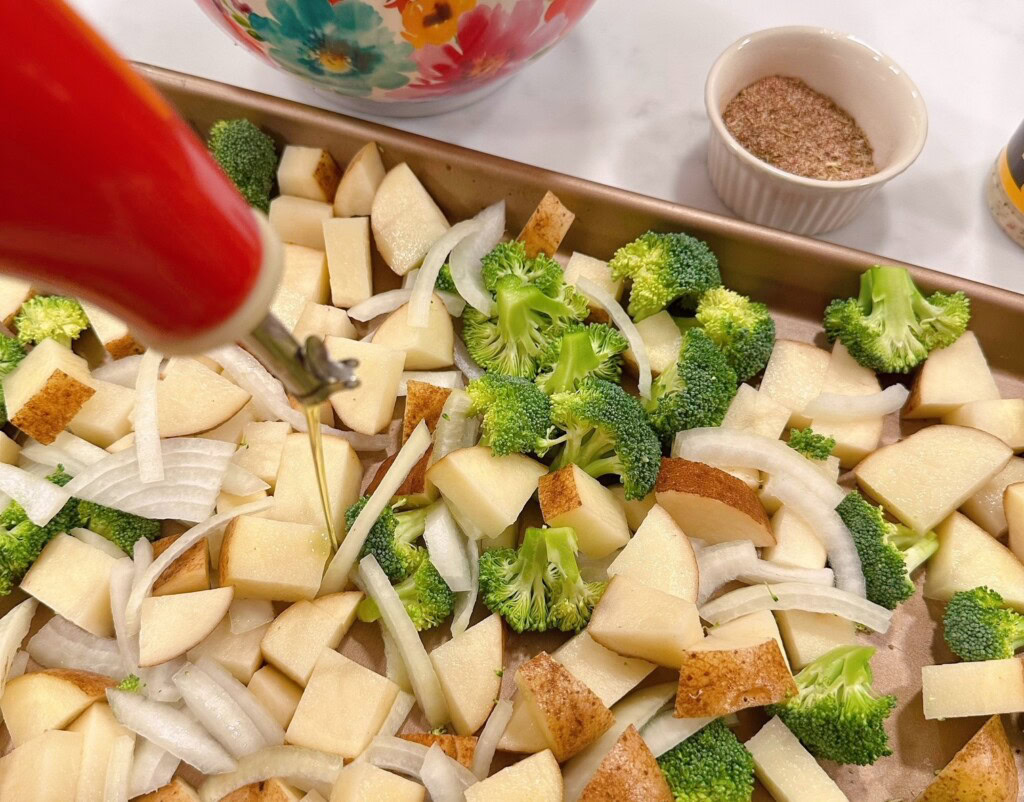 Drizzling Olive Oil over fresh cut up vegetables for sheet pan chicken dish.