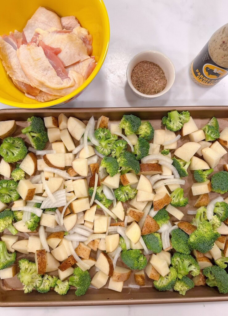 Potatoes, onions, and broccoli on a prepared sheet pan.