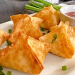 Cream cheese crab rangoons on a white serving platter with chopped green onions.
