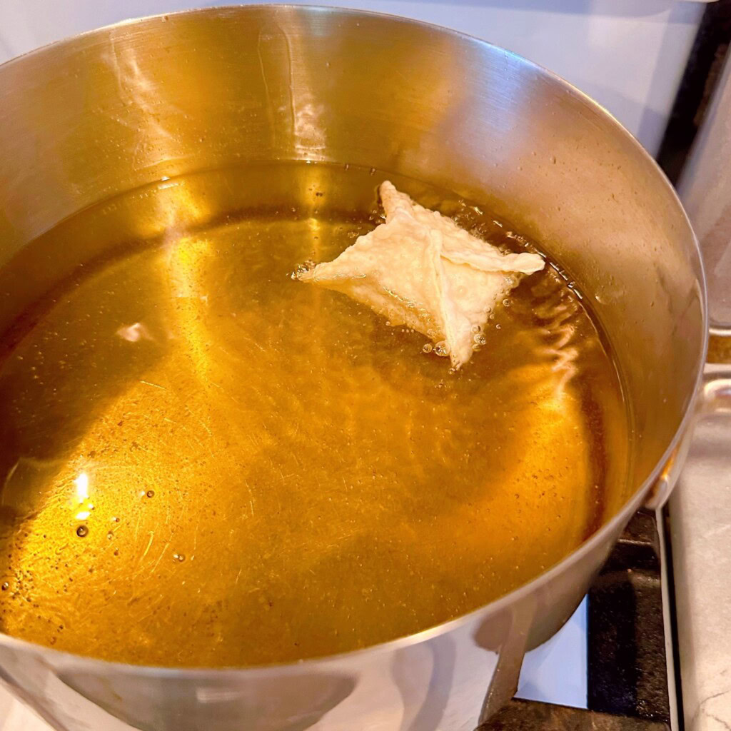 Frying wonton in heated oil in a large sauce pan on the stove top.
