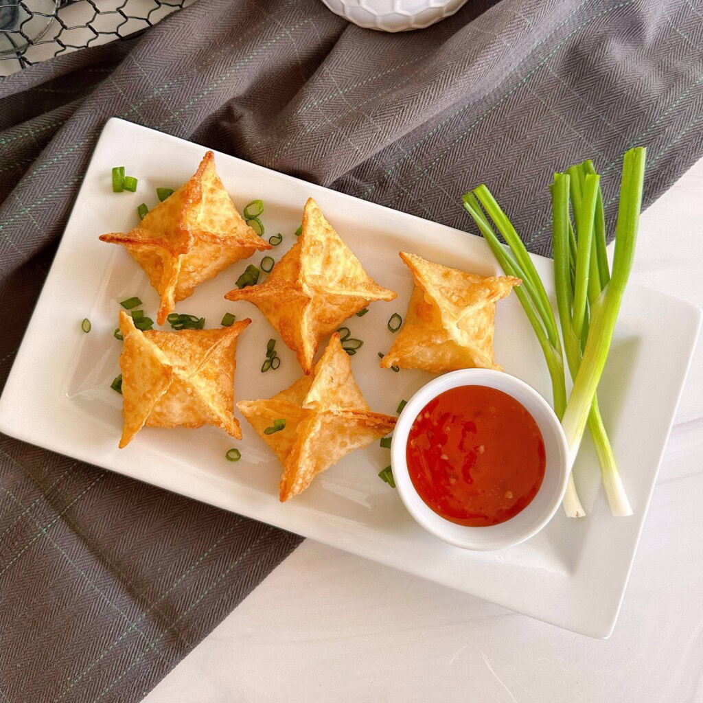 Fried wontons on a serving plate with sweet-and-sour sauce and green onions.