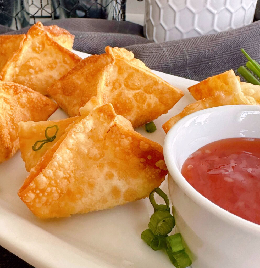 Fried cream cheese rangoons on a platter with dipping sauce.