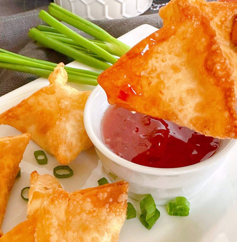 Crispy fried rangoon being dipped in sweet-and-sour sauce.