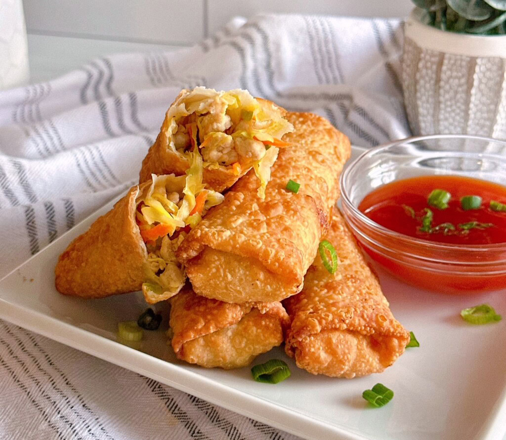 Pork Egg Rolls stacked on a plate with a side of sweet and sour sauce.