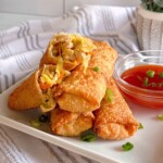 Pork Egg Rolls stacked on a plate with a side of sweet and sour sauce.