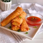 Simple Pork Egg rolls stacked on a white plate with sweet and sour sauce.