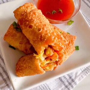 Egg Rolls on a white plate with sweet and sour sauce on the egg rolls.