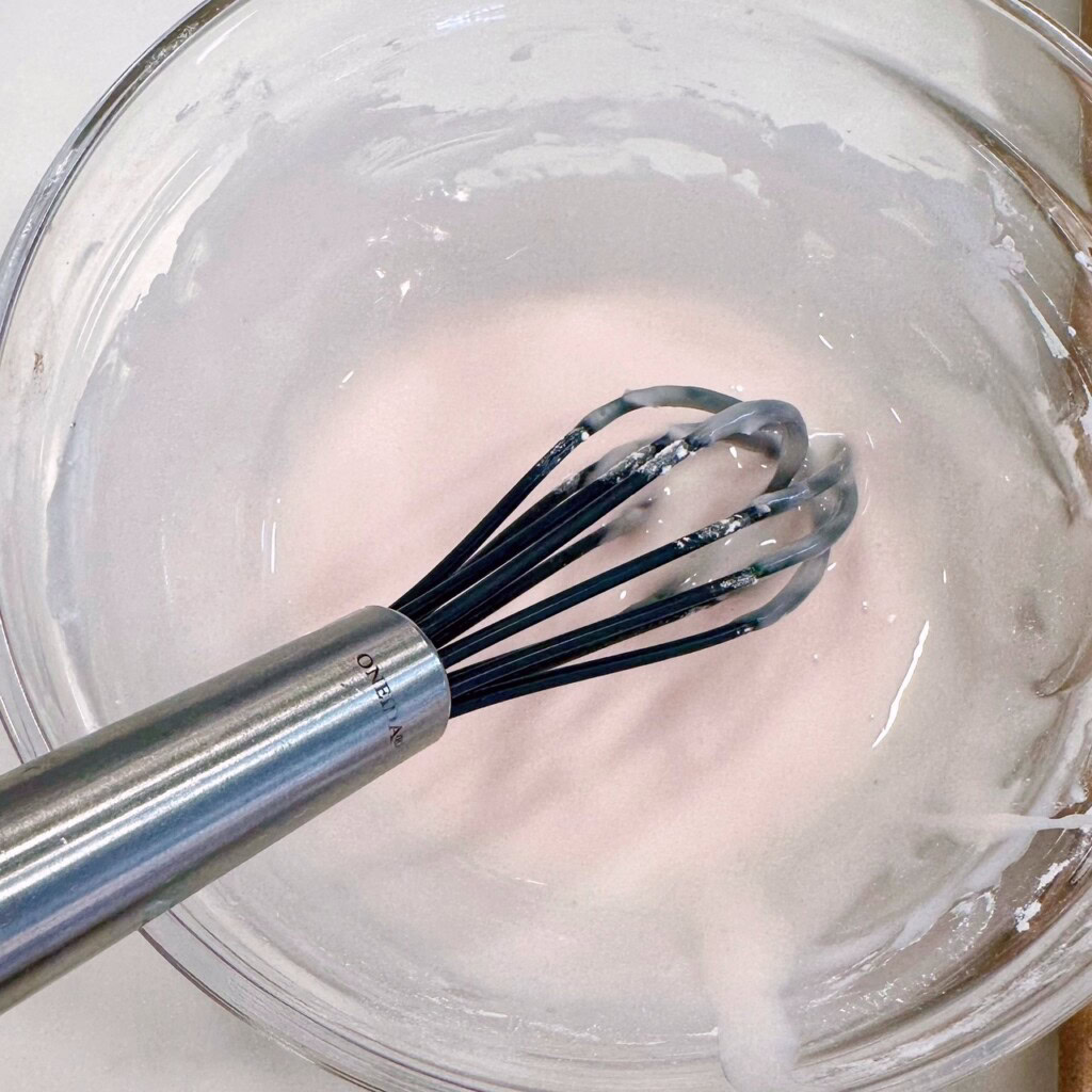 Strawberry glaze in a small bowl with a wire whisk.