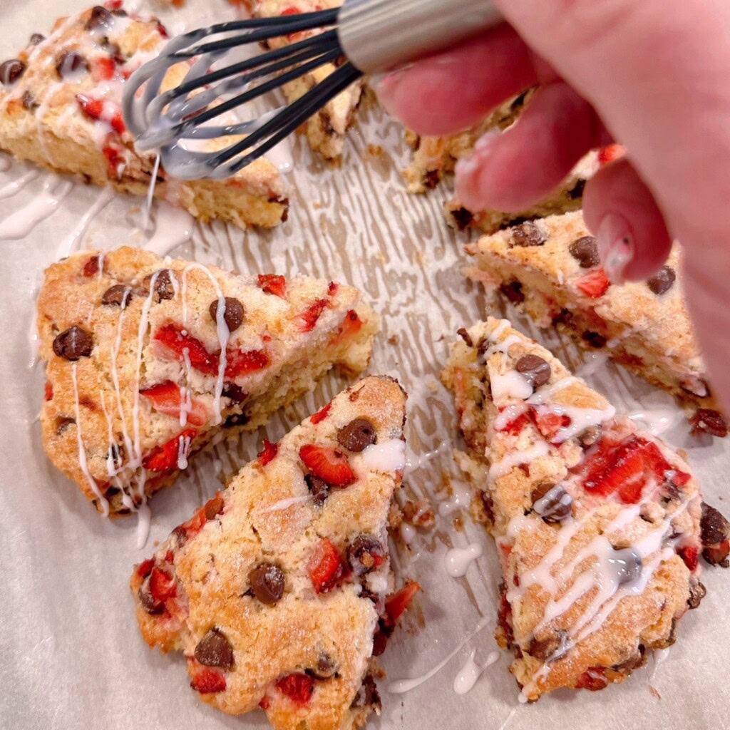 Drizzling strawberry glaze over scones with a small wire whisk.