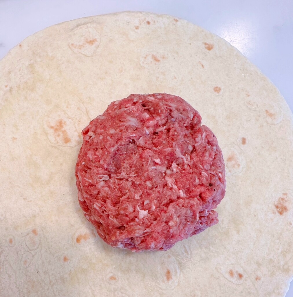 Placing prepared hamburger meat on flour tortillas.