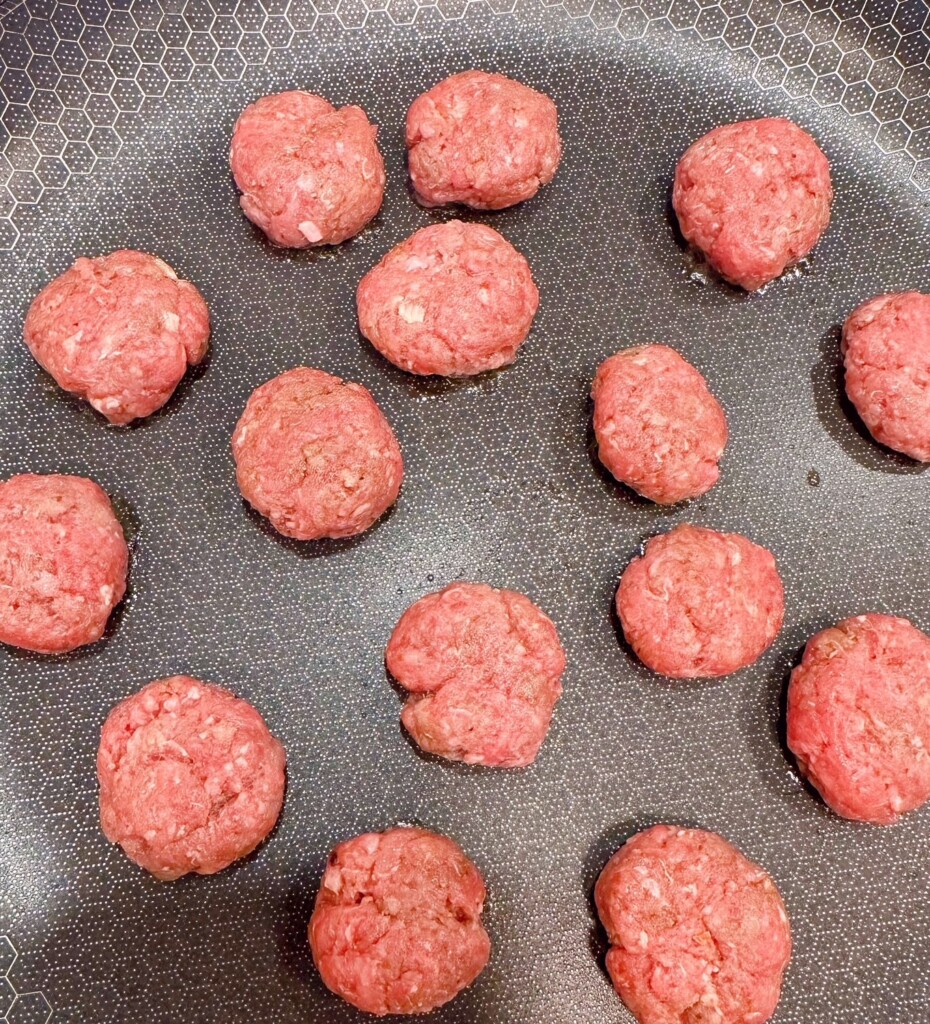 Shaped mini hamburger patties in a large skillet.