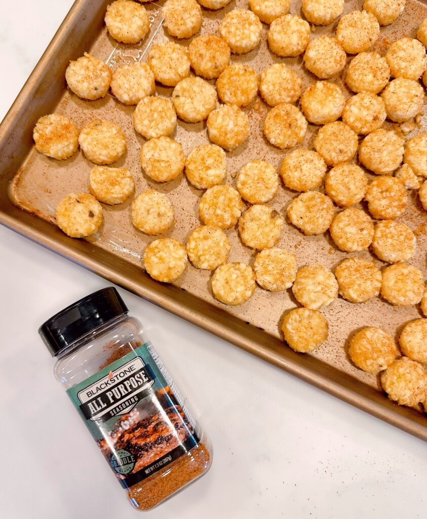 Arranging Tater Tots on large baking sheet with a jar of all-purpose seasoning mix.
