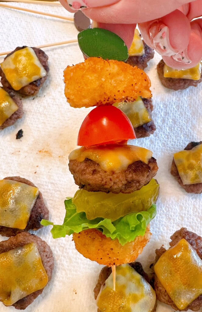Assembling mini cheeseburger bites on skewers.