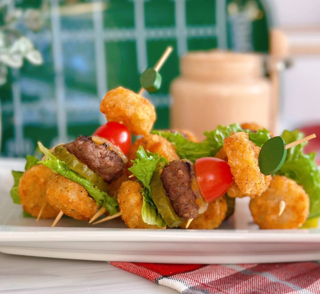 Mini Tater Tot Cheeseburger sliders on skewers, served on a white platter.