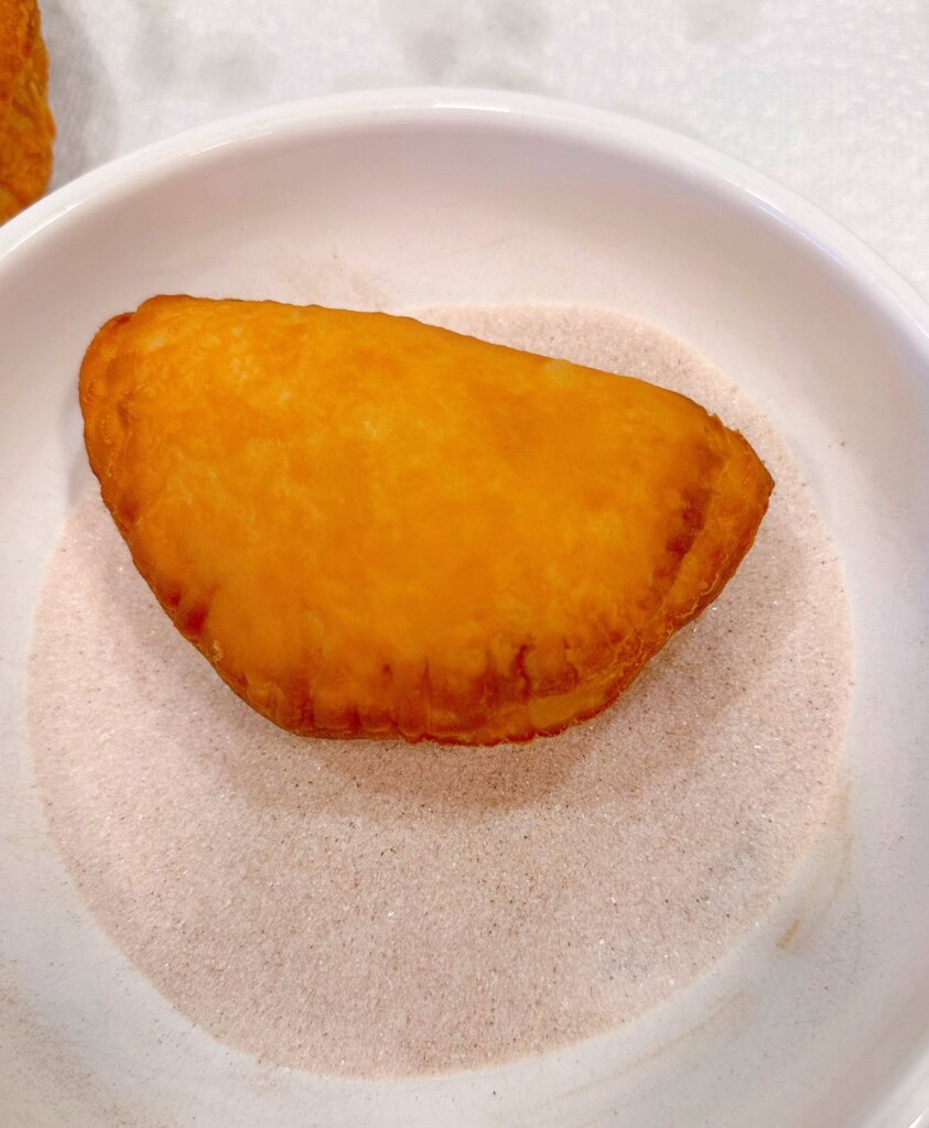 Rolling fried hand pie in cinnamon sugar.