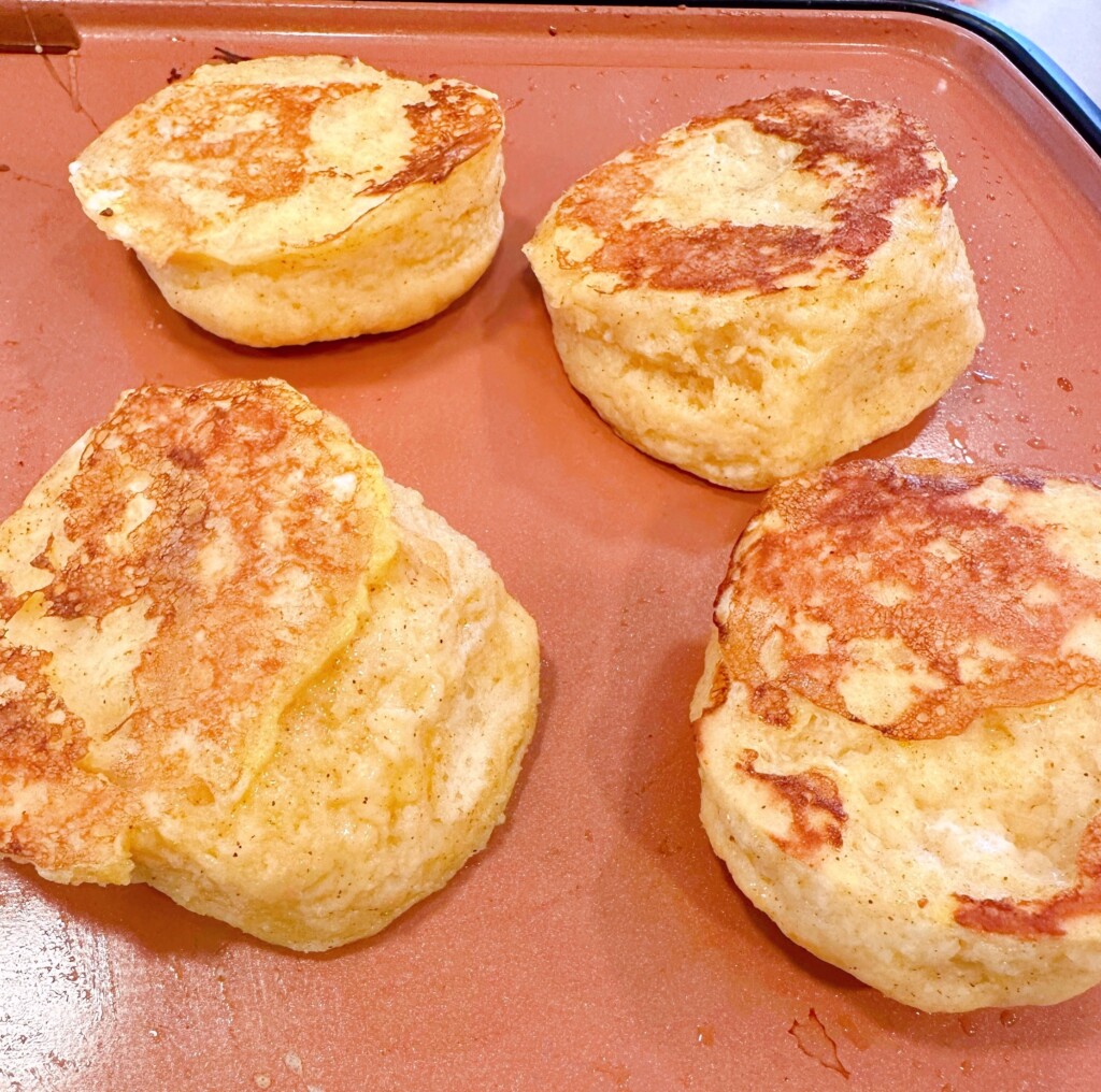Biscuits on a hot griddle cooking until golden brown.