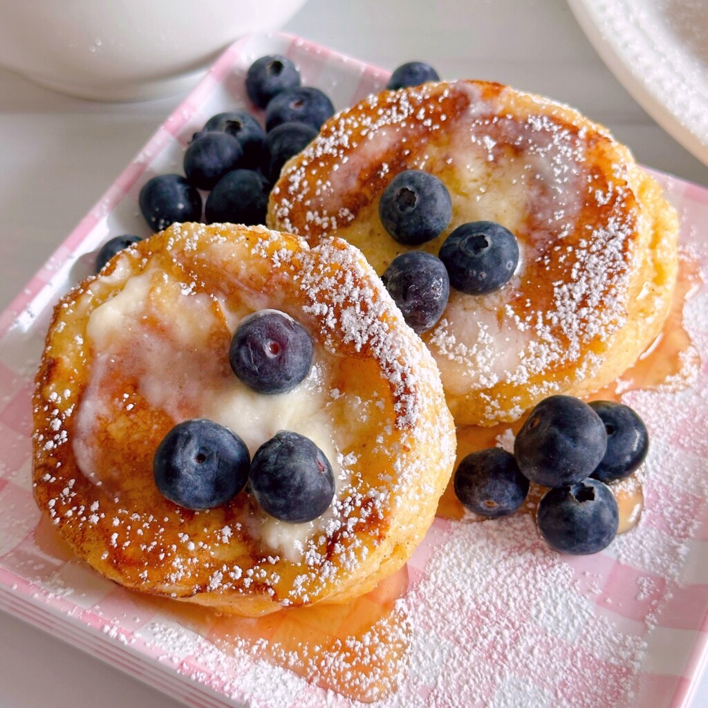 Biscuit French Toast with two slices of toast with butter, syrup, and fresh blueberries on a pink plaid plate.