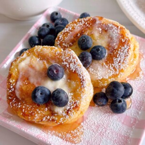 Biscuit French Toast with two slices of toast with butter, syrup, and fresh blueberries on a pink plaid plate.