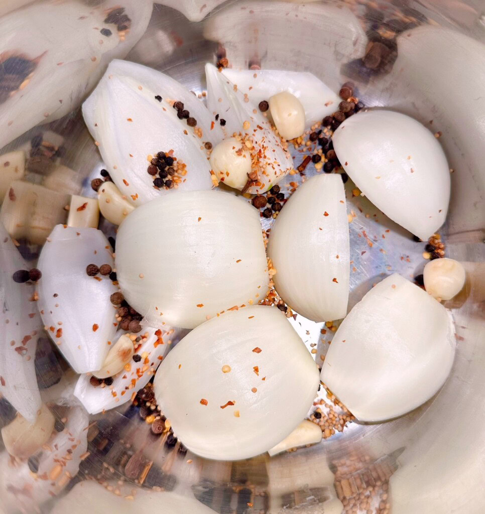 Onions, garlic cloves, and seasoning mix in the bottom of the Instant Pot.