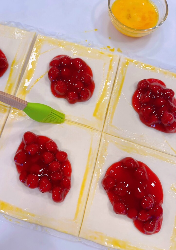 Brushing egg wash around the outside edge of each square.