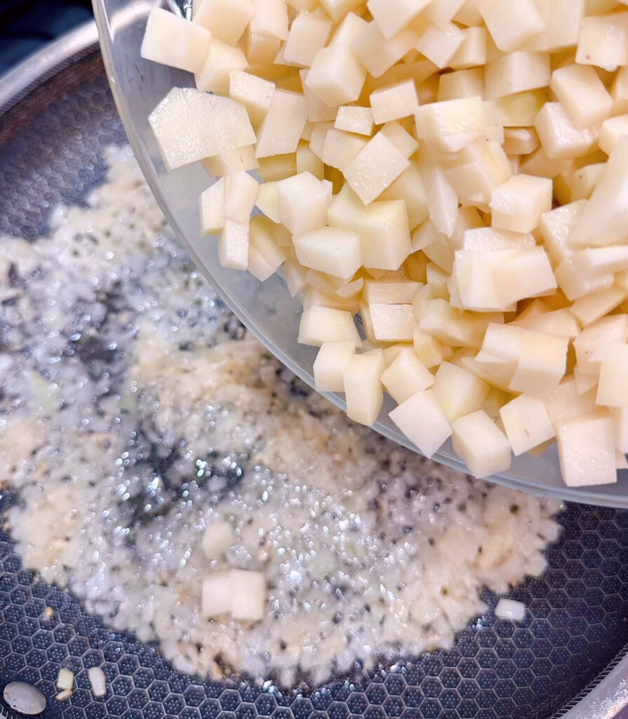 Adding potatoes to onions and garlic in large skillet.