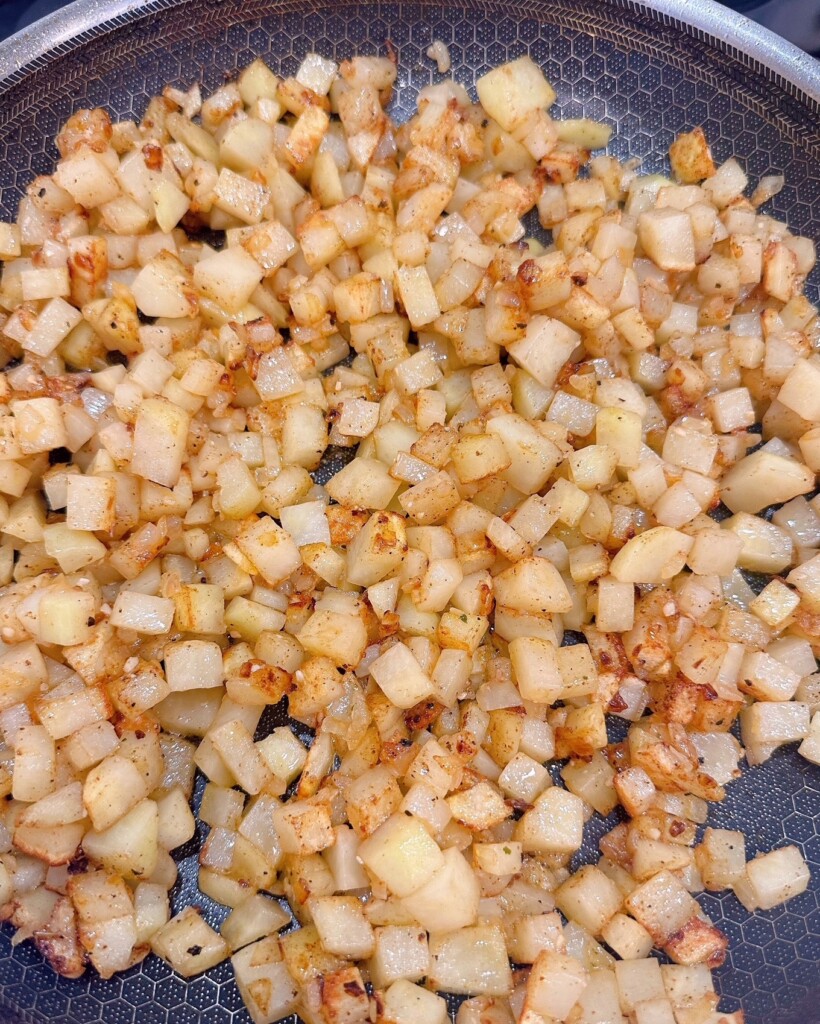 Potatoes cooking in the skillet on the stove top.