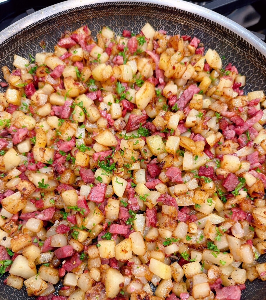 Cooked corn beef hash with chopped parsley in a large skillet.