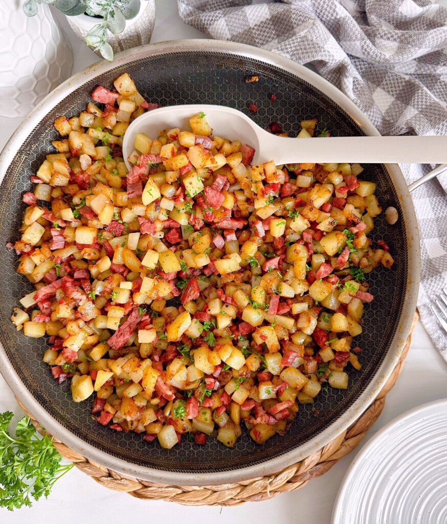Corned Beef Hash in a skillet with a serving spoon on kitchen counter top.