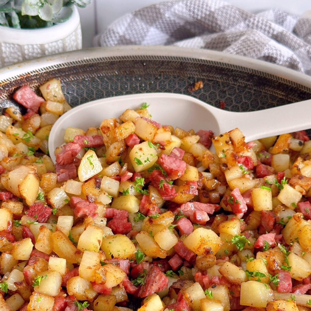 Close-up of corned beef hash in a serving spoon inside a skillet.