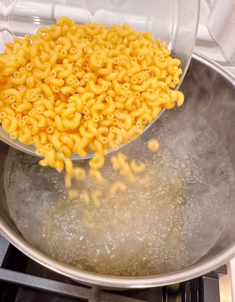 Adding macaroni to boiling water in a large pot.