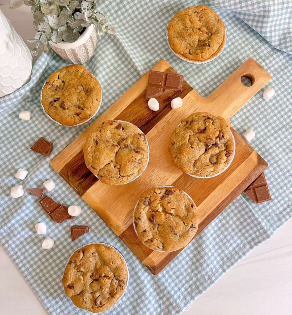 Over head shot of S'mores mini chocolate chip pies on a cutting board surrounded by chocolate and marshmallows.