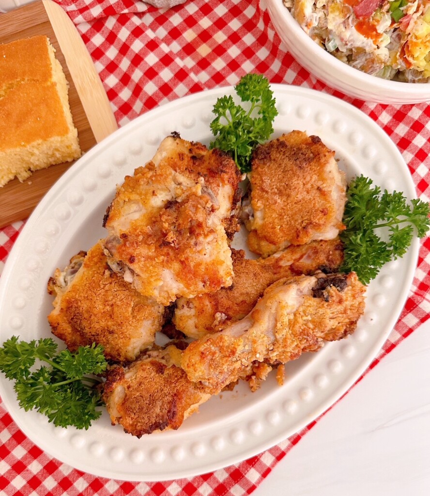 Bisquick Oven Fried Crunchy Chicken on a serving platter surrounded by cornbread and a potato salad.