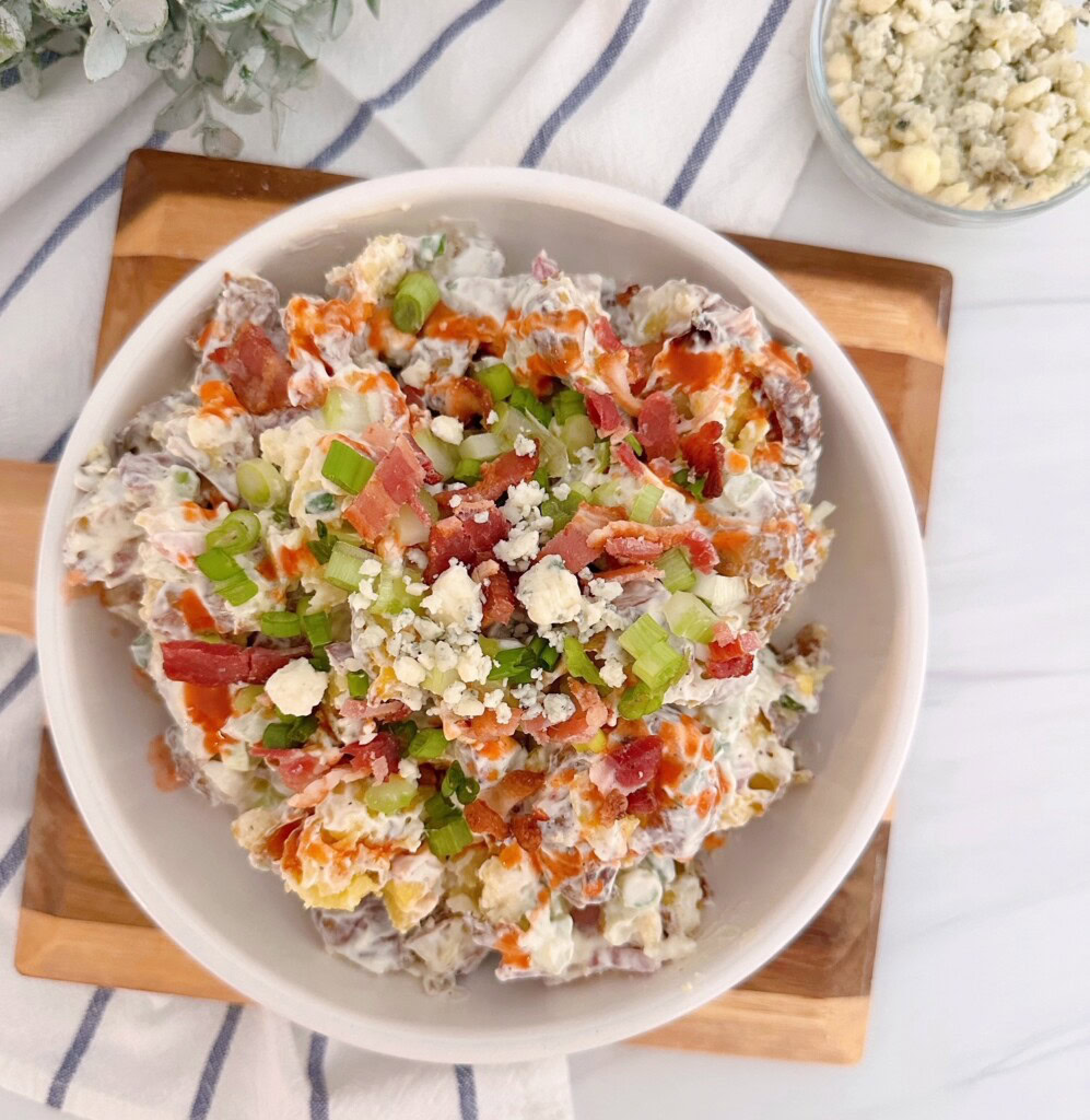 Smashed Buffalo Potato salad in a bowl on a cutting board with a bowl of blue cheese sitting by the side.