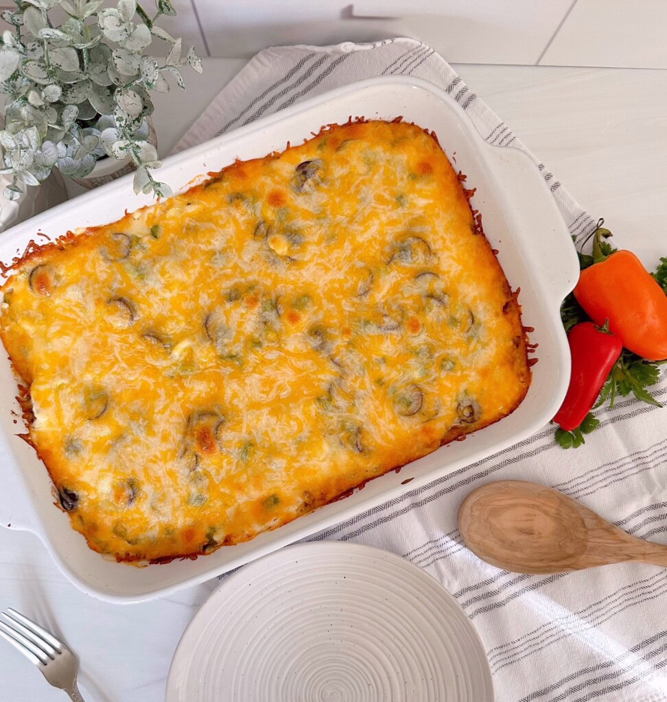 Taco Casserole out of the oven in the casserole dish with melted cheese, peppers and a wooden spoon.