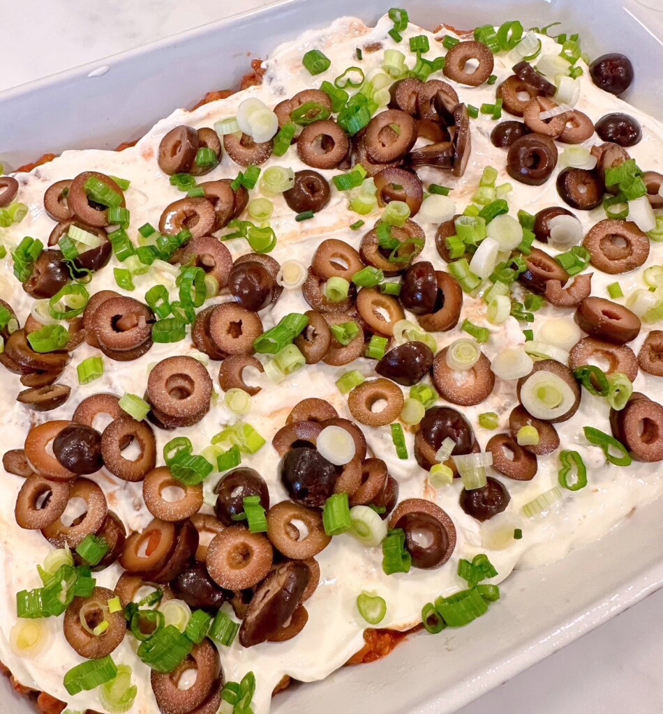 Sour cream with chopped green onions and sliced olives on top of meat mixture.