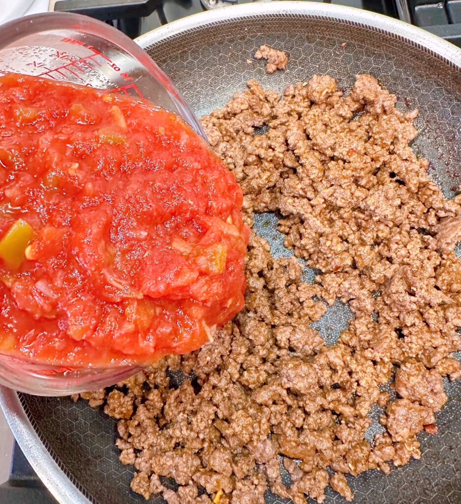 Adding Salsa to ground beef mixture in large skillet.