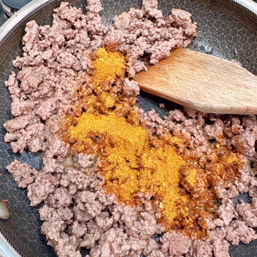 Browning ground beef in a large skillet and adding taco seasoning packet.