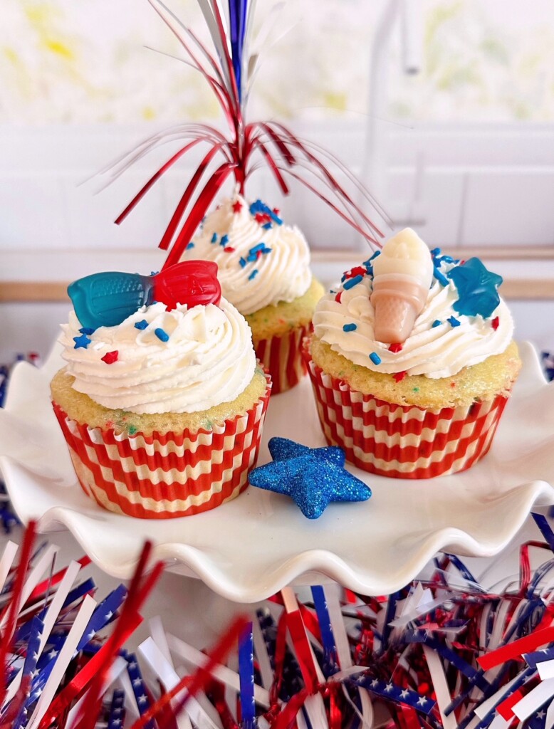 Three decorated cupcakes on a white cake stand.