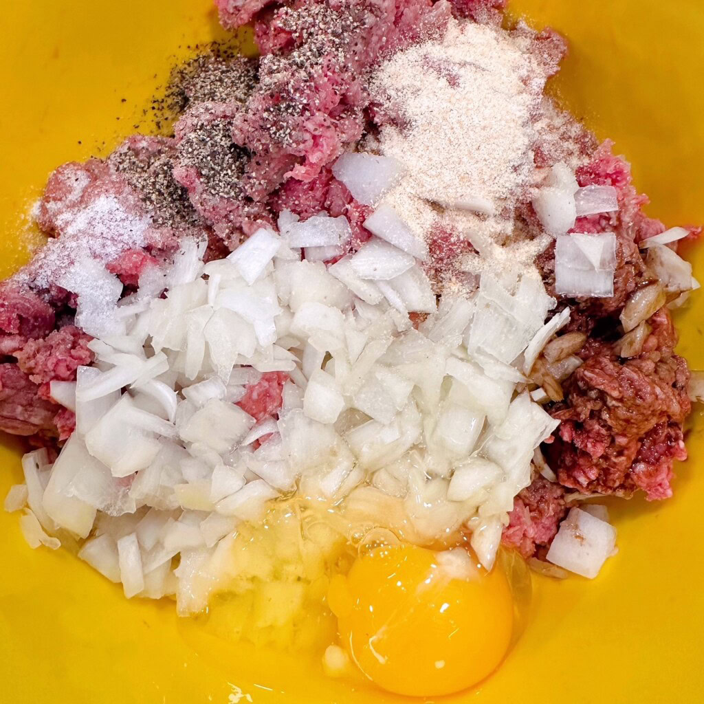 Ingredients for hamburger patties in a yellow mixing bowl.