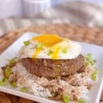 Up close Loco Moco on a serving plate with gravy and rice. Yolk running down the meat patty.