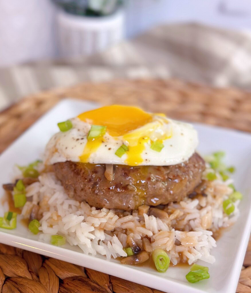 Up close Loco Moco on a serving plate with gravy and rice. Yolk running down the meat patty.