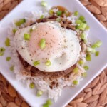 Adding the eggs and green onion garnish to the loco moco.