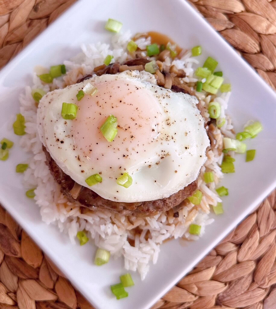 Adding the eggs and green onion garnish to the loco moco.