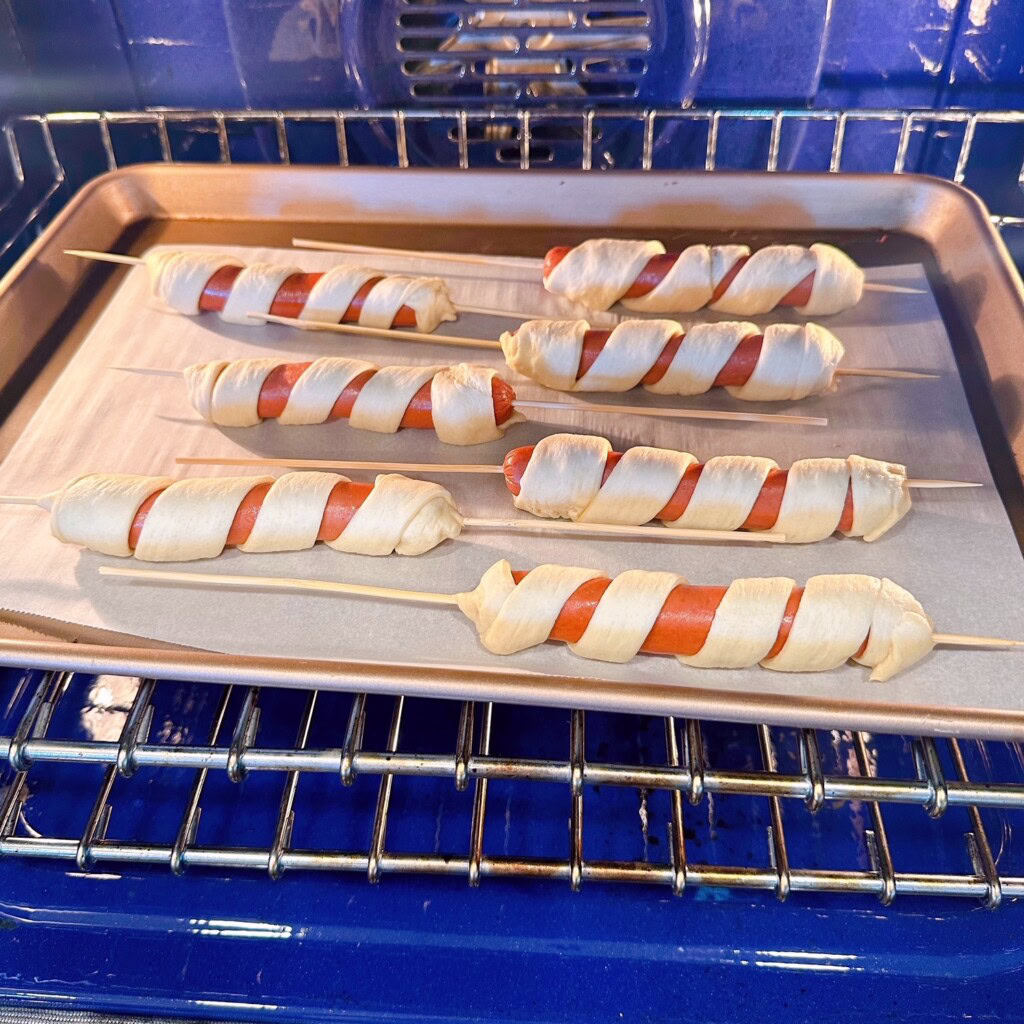 Hot Dogs on parchment lined baking sheet in the oven to bake.