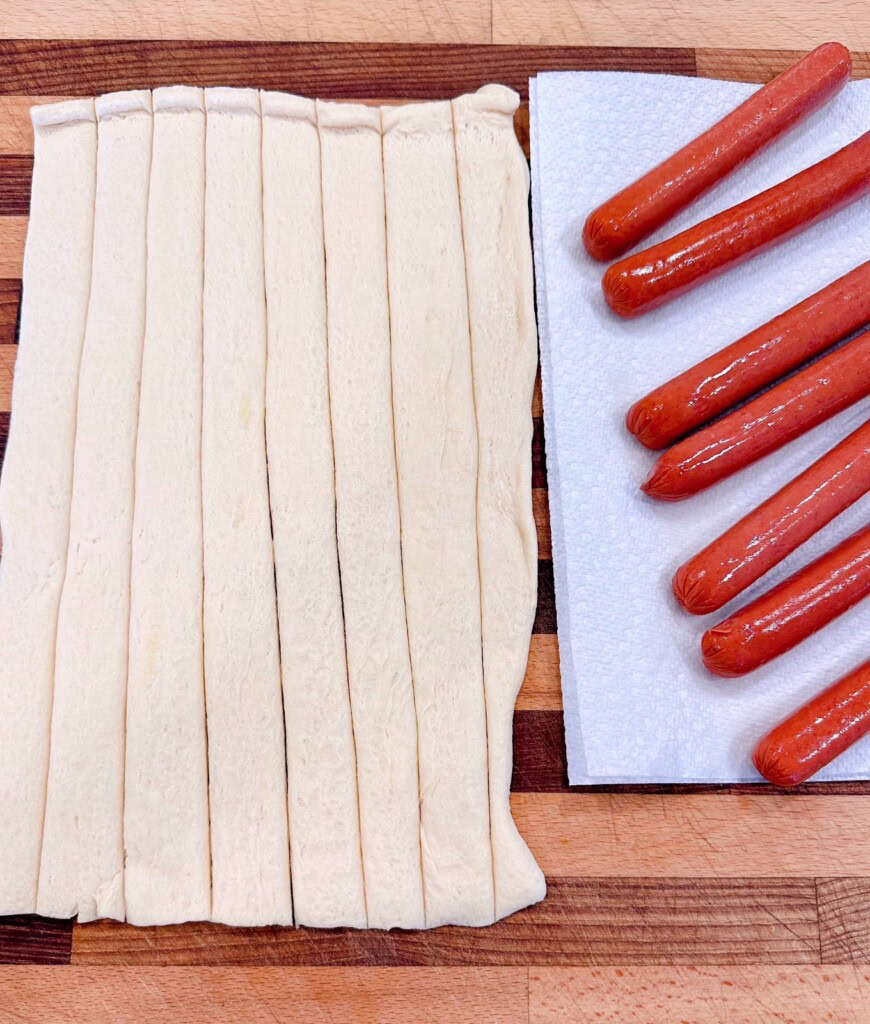 Cut crescent dough and hot dogs on a paper towel.